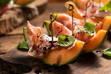 Sliced melon with ham and basil leaves, served on a wood chopping board