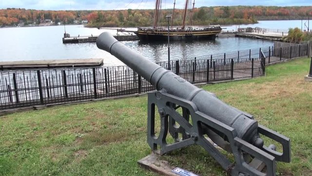 An old cannon on the shore and a two-masted ship on the pier