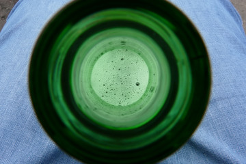 View of beer through the neck of the bottle. A bottle between the legs of a man dressed in jeans.