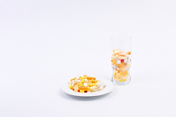 Different medicines and vitamins on a white background in a glass and a plate. Free space for text.