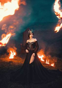 dark queen of night, majestic priestess in long black dress with bare shoulders, the witch raven in flame, powerful devil with pale skin and metal cold crown on her head, mistress and fire goddess