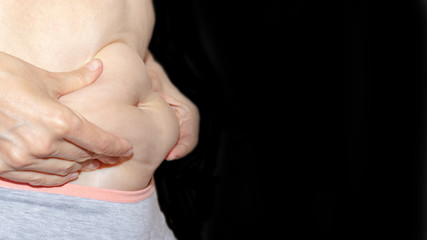 Woman holding her fat eblly, stomach with hands on black background with copy space for text, diet, weight loss and liposuction concept