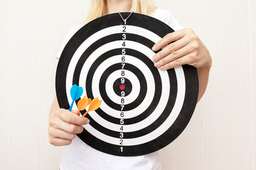 Woman holding a dart board and darts in hands close up, aiming and targetting in business and life...