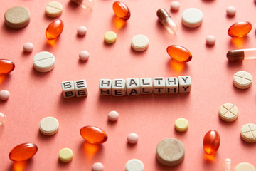 Black and white title BE HEALTHY from white cubes on the table with tablets on coral background