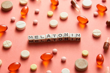 Black and white title MELATONIN from white cubes on the table with tablets on coral background