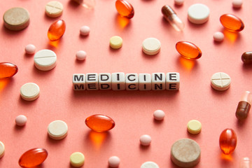 Black and white title MEDICINE from white cubes on the table with tablets on coral background