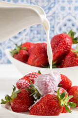 Close up, macro. Someone pours milk (cream) into a plate of delicious red strawberries.