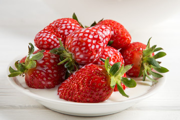 Close up. Juicy red strawberry berries are filled with cream (milk) in a white porcelain plate.