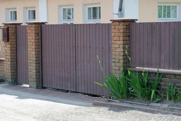 Fototapeta premium a large brown gate and part of a fence made of metal and bricks outside in green vegetation