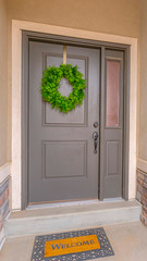 Vertical Gray front door of a home with a simple green wreath and sidelight