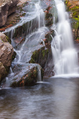 Fototapeta premium Gorgeous mountain creek waterfall cascading down the rocky cliff and colorful autumn red leaves, close-up