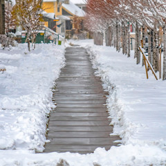 Square Wooden pathway amid trees and homes in Daybreak Utah viewed in winter