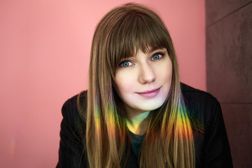 Portrait of a happy blonde long-haired woman posing on a pink background sitting against the wall with prismatic effect sun spot on her hair in city cafe.