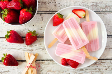 Healthy strawberry yogurt ice pops on a plate, top view table scene against a white wood background