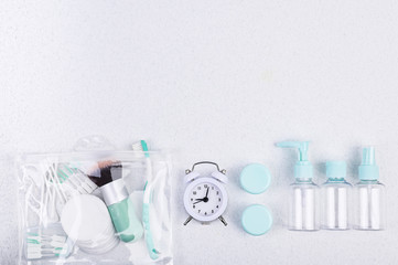 Plastic containers, toothbrush and alarm clock for travel on a white background. Flat lay