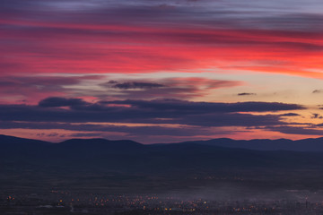 Dramatic, colorful late blue hour sky above distant city covered in mist and silhouette horizon mountains - 268425729