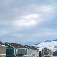 Square Row of homes against snow covered mountain under the cloud filled sky