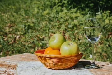 A glass of fresh Apple water and apples in a basket on a wooden table.