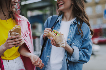 Two happy female friends eating hot dogs by walk