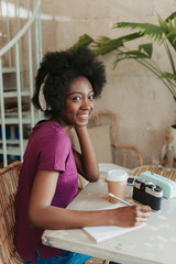 Fototapeta na wymiar Waist up of happy African woman in headphones spending time in cafeteria