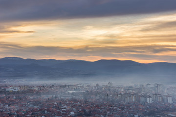 Stunning, soft view of golden sunset sky above scenic cityscape covered by haze and mist
