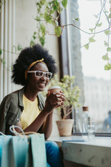 Low angle of smiling African lady drinking coffee in cafe