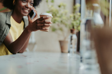 Low angle of happy African lady drinking coffee in cafe