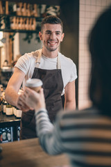 Waist up of friendly barista smiling to the cafe visitor - obrazy, fototapety, plakaty