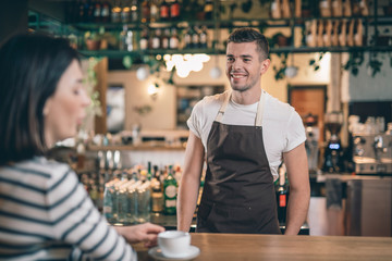Cheerful barista standing at the bar counter and smiling