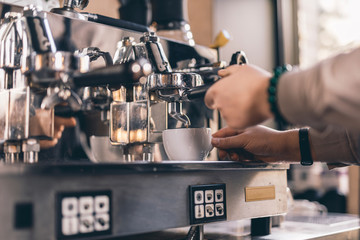 Hand of barista putting cup on the tray of espresso machine