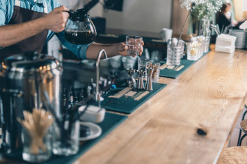 Hands of man taking clean glass and holding coffee jug