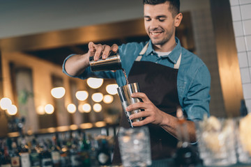 Positive young man pouring liquid into the cocktail shaker
