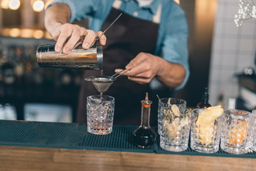 Careful bartender pouring cocktail through the strainer