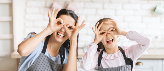 Happy Mom And Daughter In Aprons Making Glasses With Hands