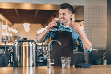 Pleased bartender smelling pour over coffee and smiling