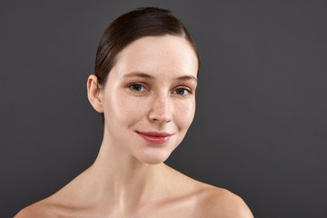 Charming girl with freckles standing against gray background