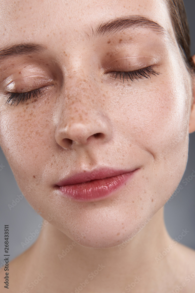 Sticker Serene pretty girl with freckles standing against gray background