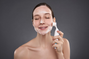 Pretty girl with closed eyes using pore cleansing brush after bath