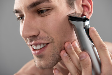 Joyful young man shaving with electric razor