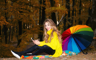 Beautiful happy smiling girl with long hair wearing stylish jacket posing in autumn day. Happy young woman in park on sunny autumn day. Beautiful young happy girl with bright red-yellow leaf in park.