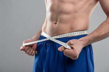 Athletic young man with perfect abs measuring his waist