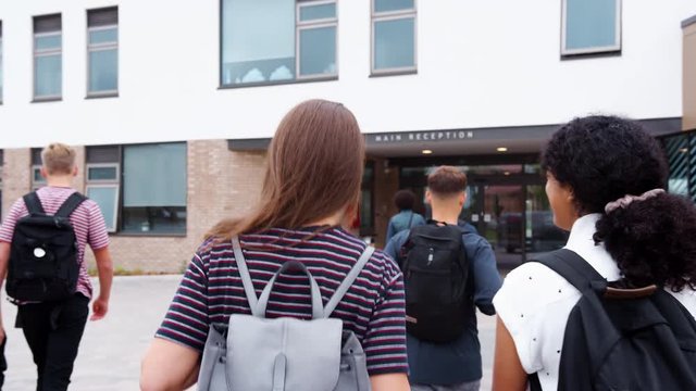 Rear View Of Two Female High School Students Walking Into College Building Together
