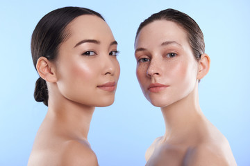 Close up portrait of two interracial attractive women situating against blue background