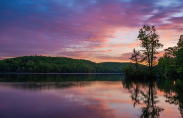 Colorful sunrise over the lake at Harriman State Park, New York, featuring trees and sky reflection on the foreground and dramatic sky on the background.