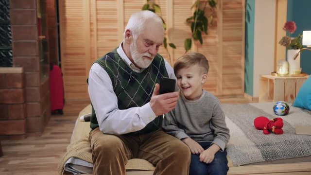 Seniour and child use smart phone at home smiling happy kid child family man grandfather grandson technology senior elderly grandpa together boy, sitting play close up slow motion