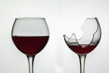 Broken and not broken wine glass with red wine on white background