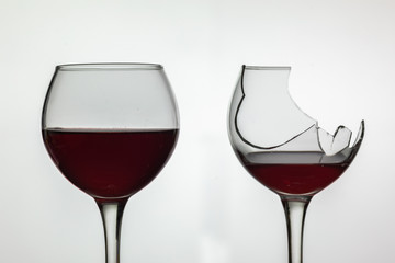 Broken and not broken wine glass with red wine on white background