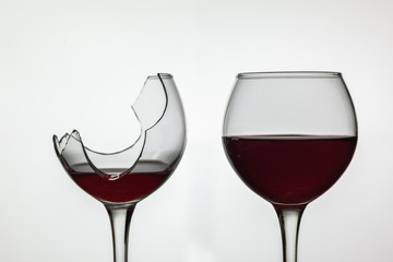 Broken and not broken wine glass with red wine on white background