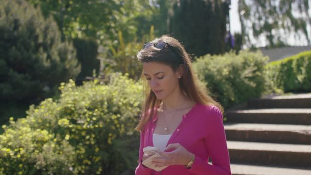Young woman on her phone walking through a nice garden area, in slow motion
