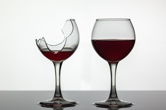 Broken and not broken wine glass with red wine on white background